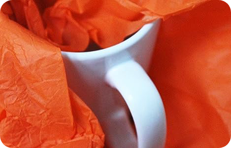 Part orange tissue paper wrapped mug showing a white handle peaking out.
