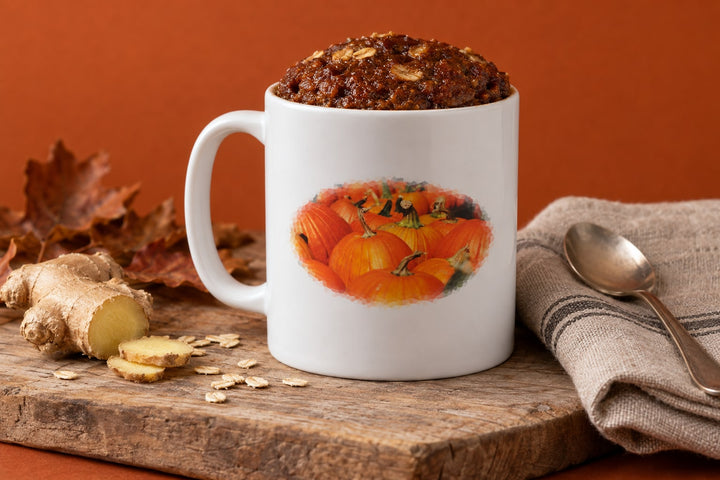 A pumpkin-patterned mug of dark, risen ginger parkin cake with a glossy domed top. A teaspoon lies on a linen napkin beside it, against a burnt-orange backdrop.